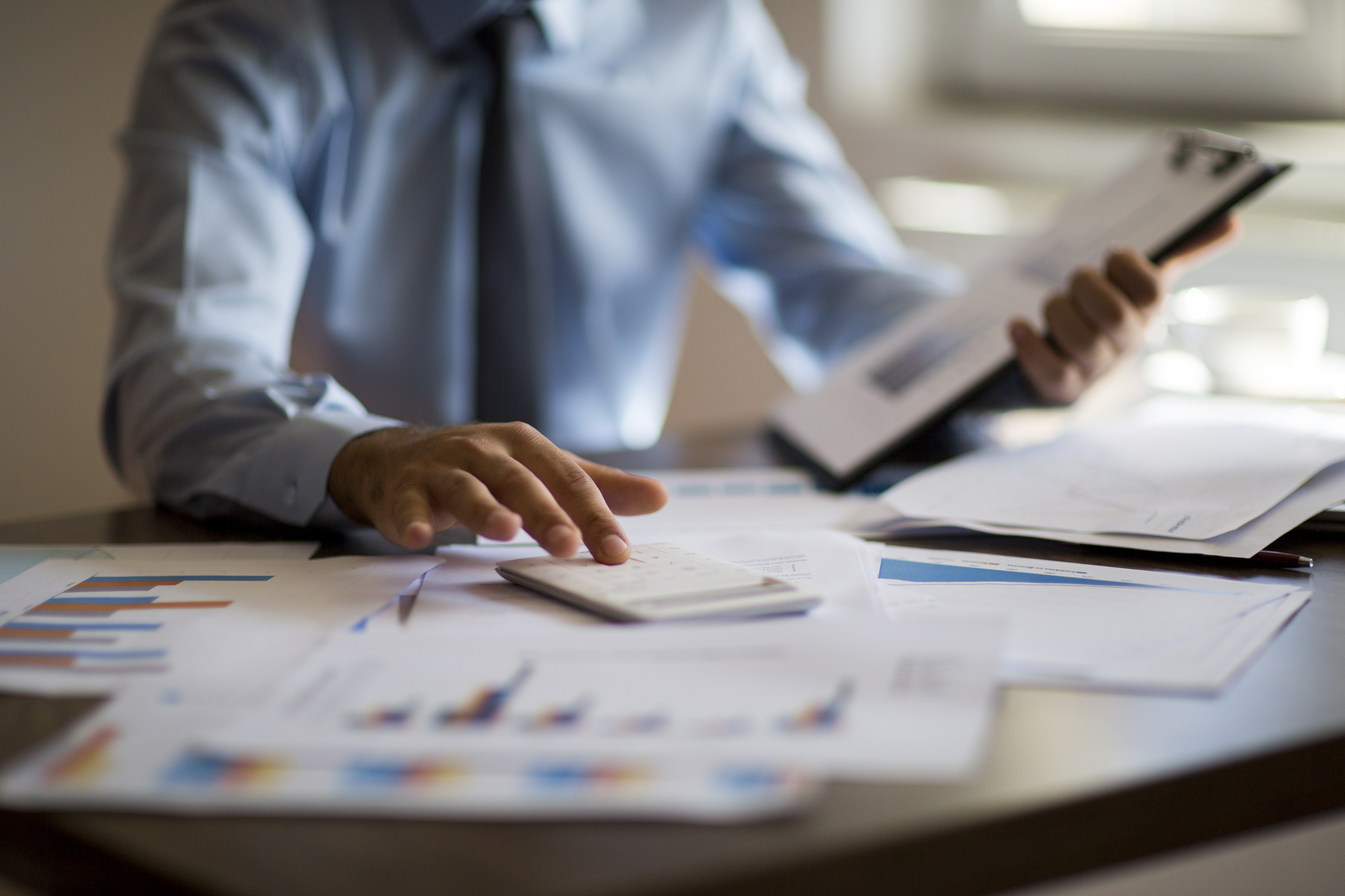 Business person using a calculator along with a laptop, budget and loan paper in their office.