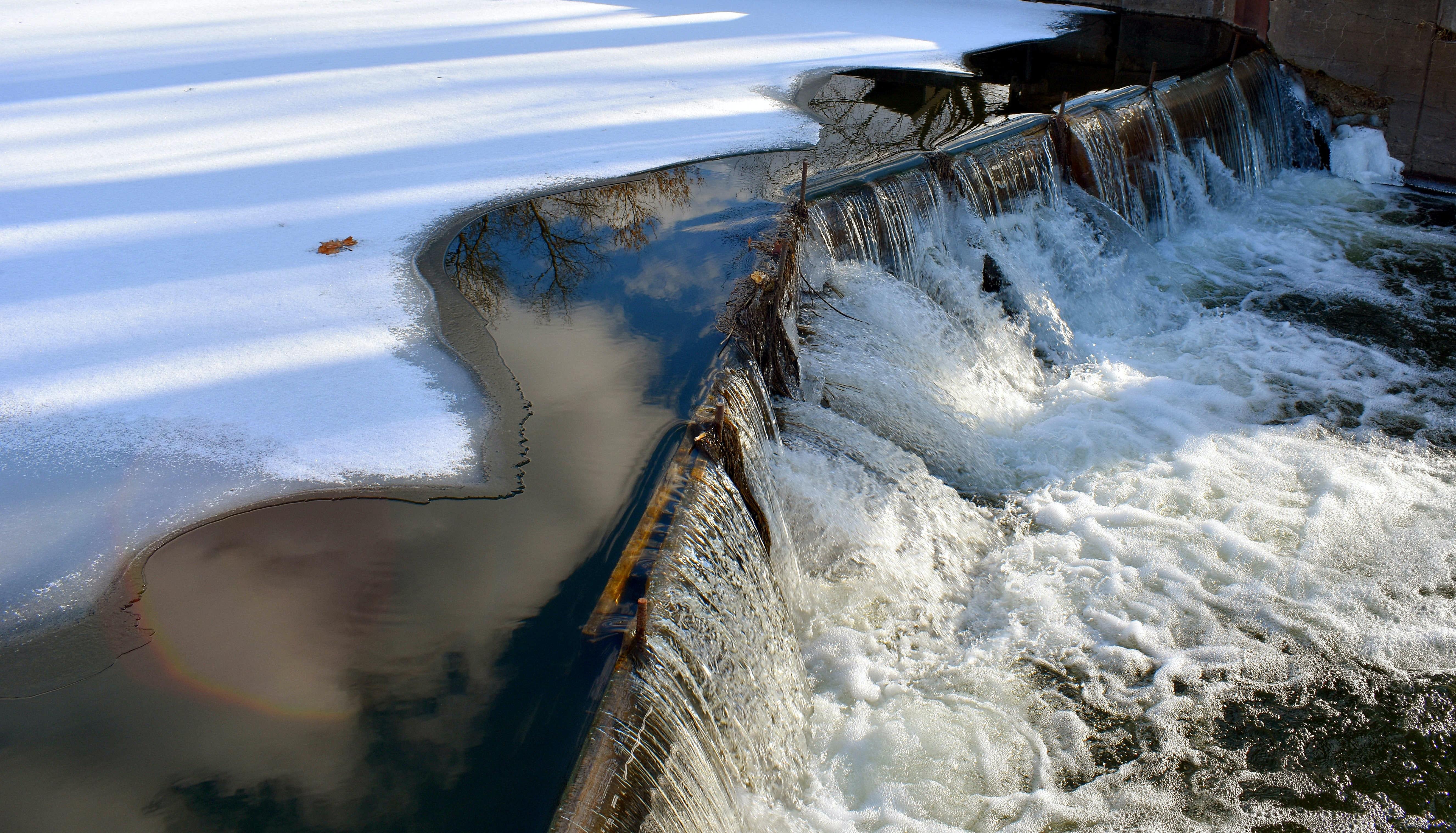 Image of water pouring over a dam from a large, ice-covered river.