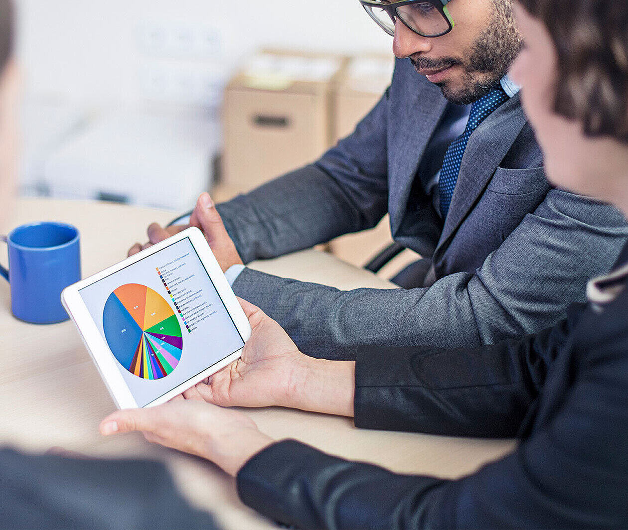 Three people sat at a table looking at charts on a tablet screen.