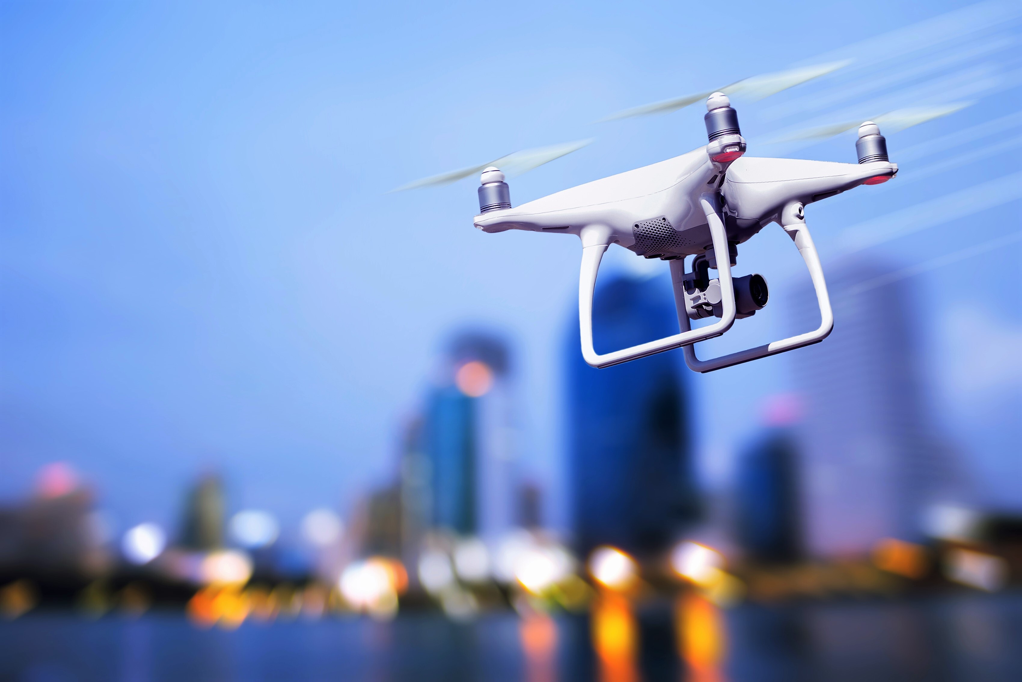 a white drone in flight across a city at dusk