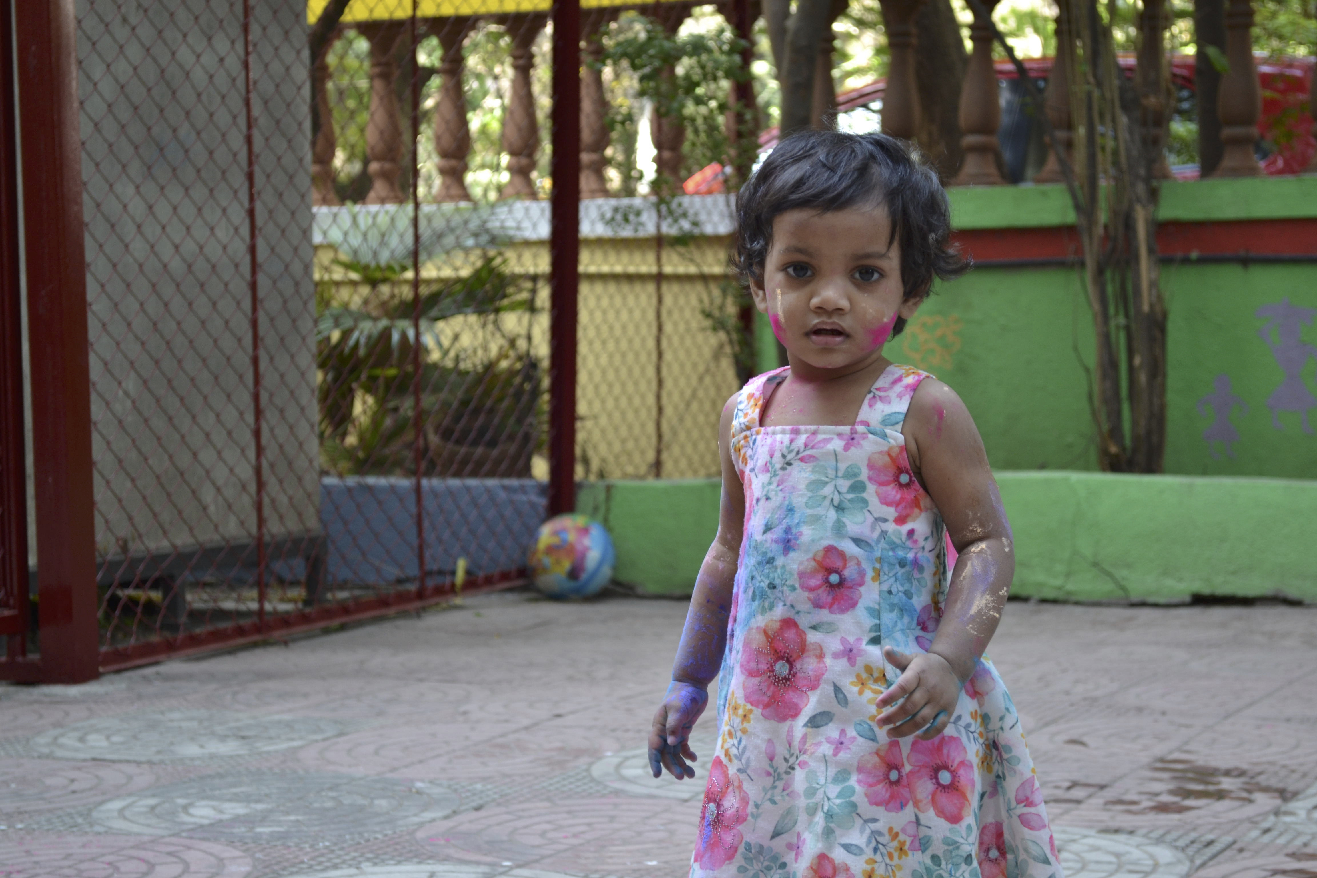 A young girl wearing a flower patterned dress is covered in paint, having played in a playground