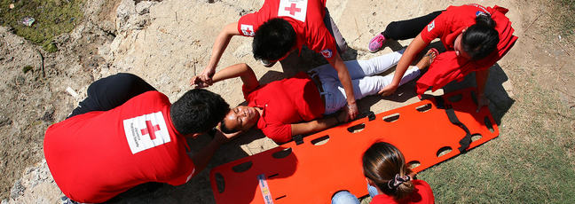 Red Cross First Aid workers help a teenage girl onto a stretcher.