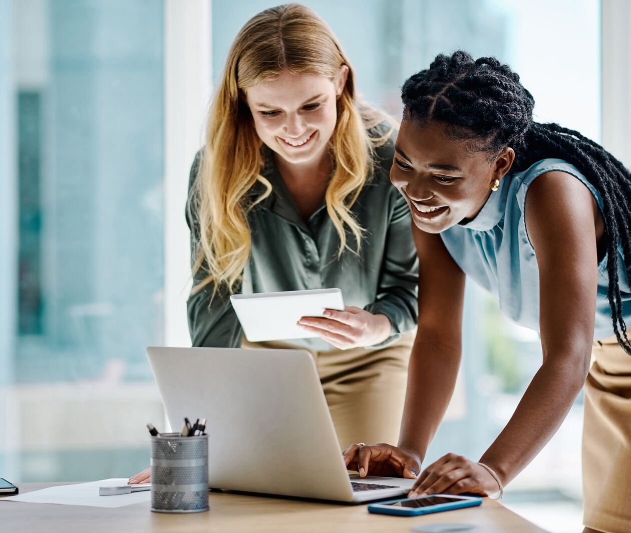 Two women at work looking at a screen together working on a task smiling