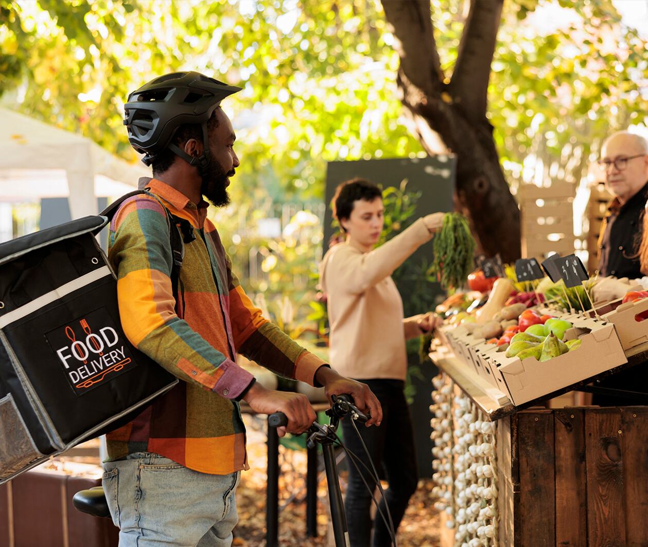 Business man riding his food delivery bicycle stops for food delivery or pickup from community food market