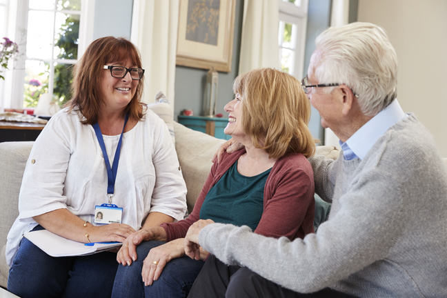 A healthcare worker sitting on a couch talking to an older couple.