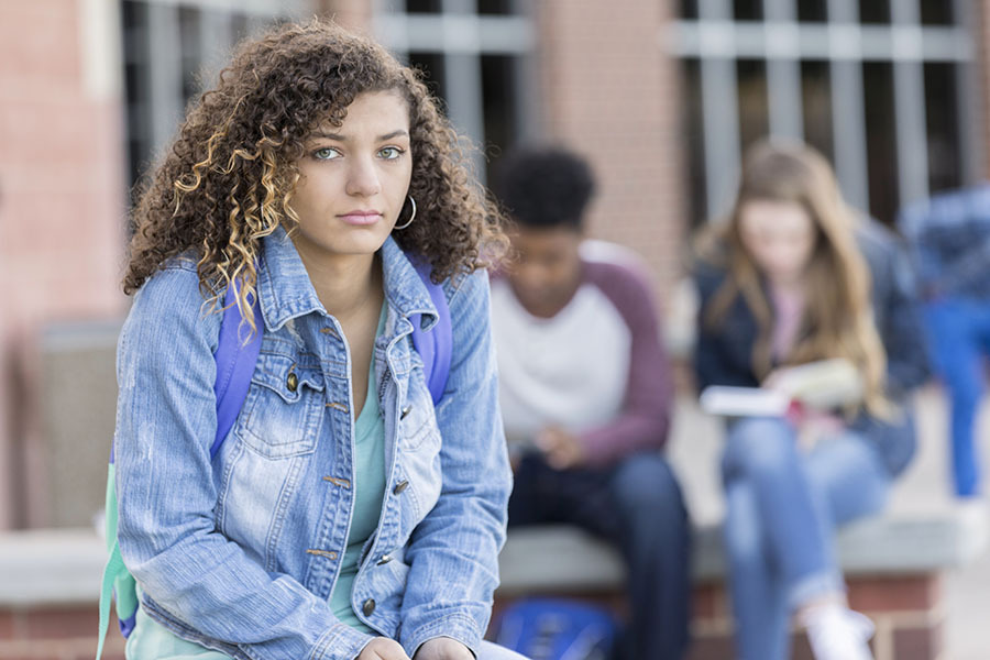 Girl sitting away from friends looking anxious