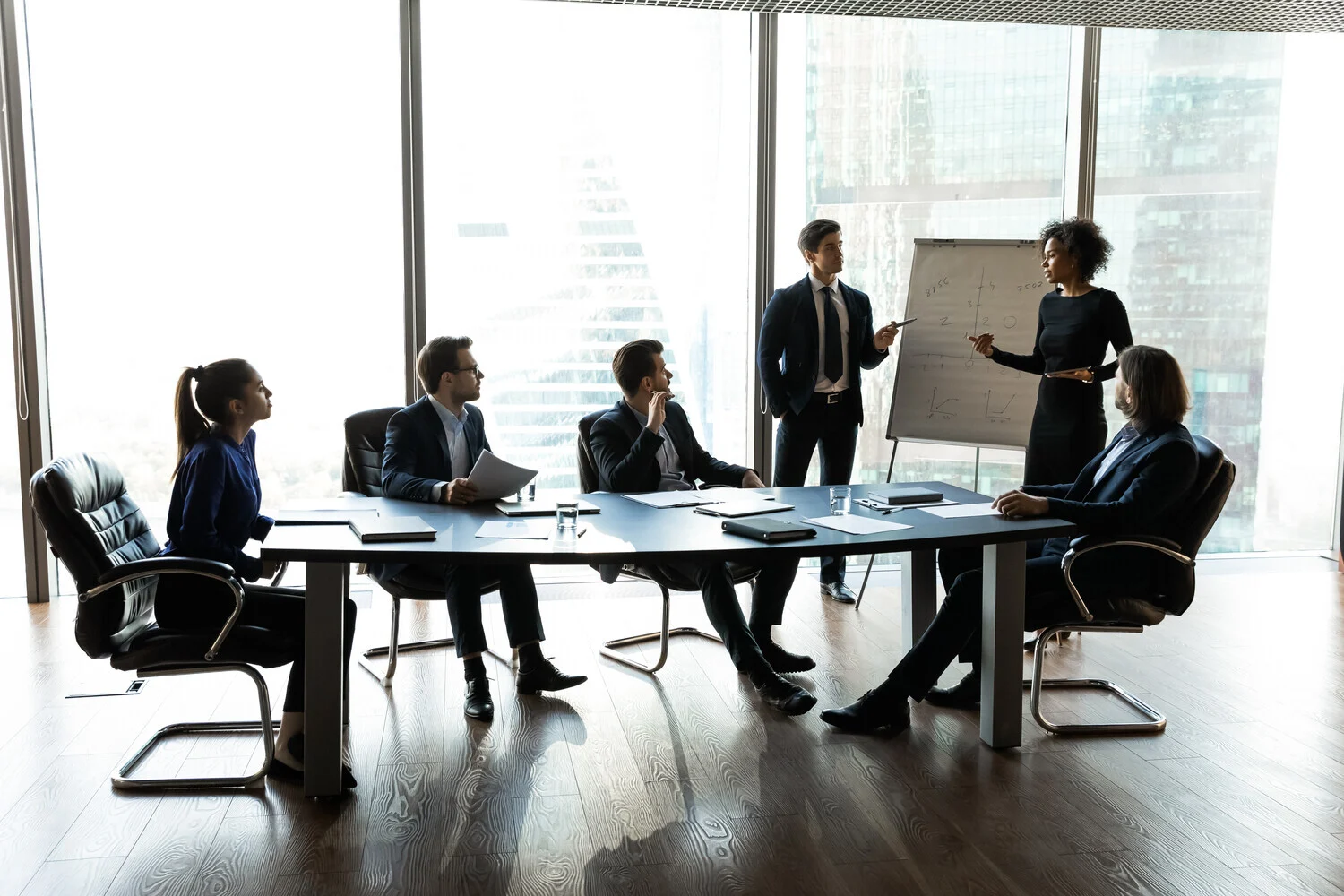 Image of six people discussing ideas around a table and white board