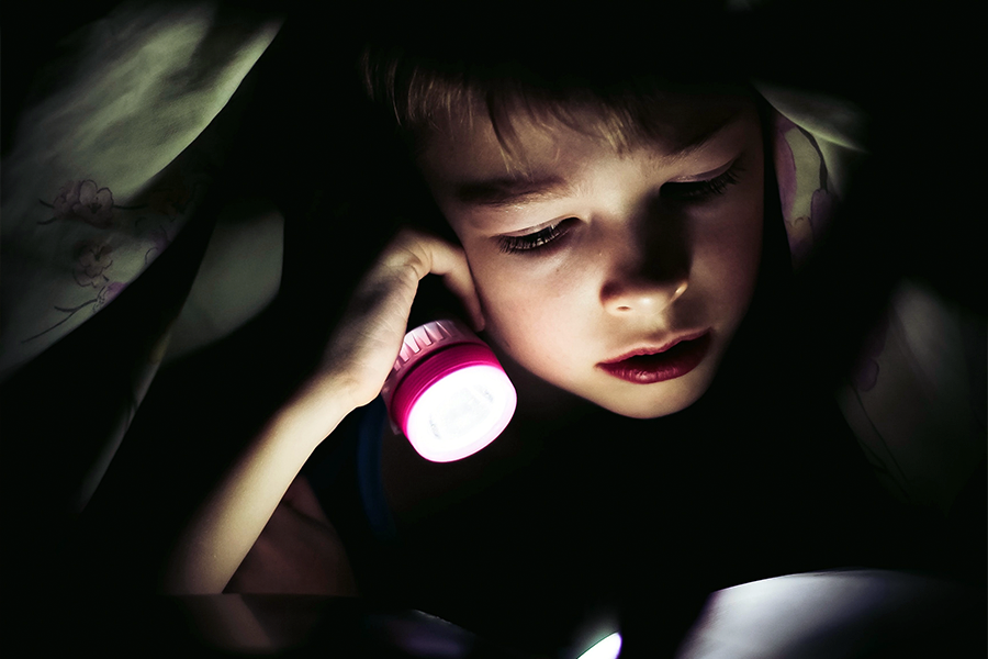 Young boy reading book by torchlight