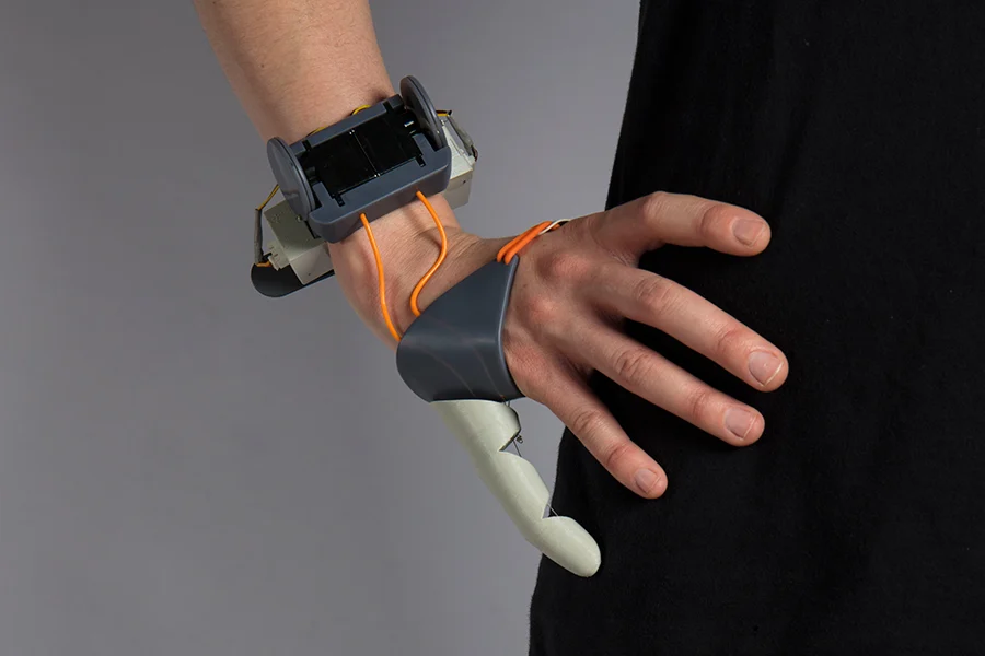 Decorative image, hand wearing a mechanical device that gives the wearer an extra finger or thumb for increased mobility. By Dani Clode, The Third Thumb