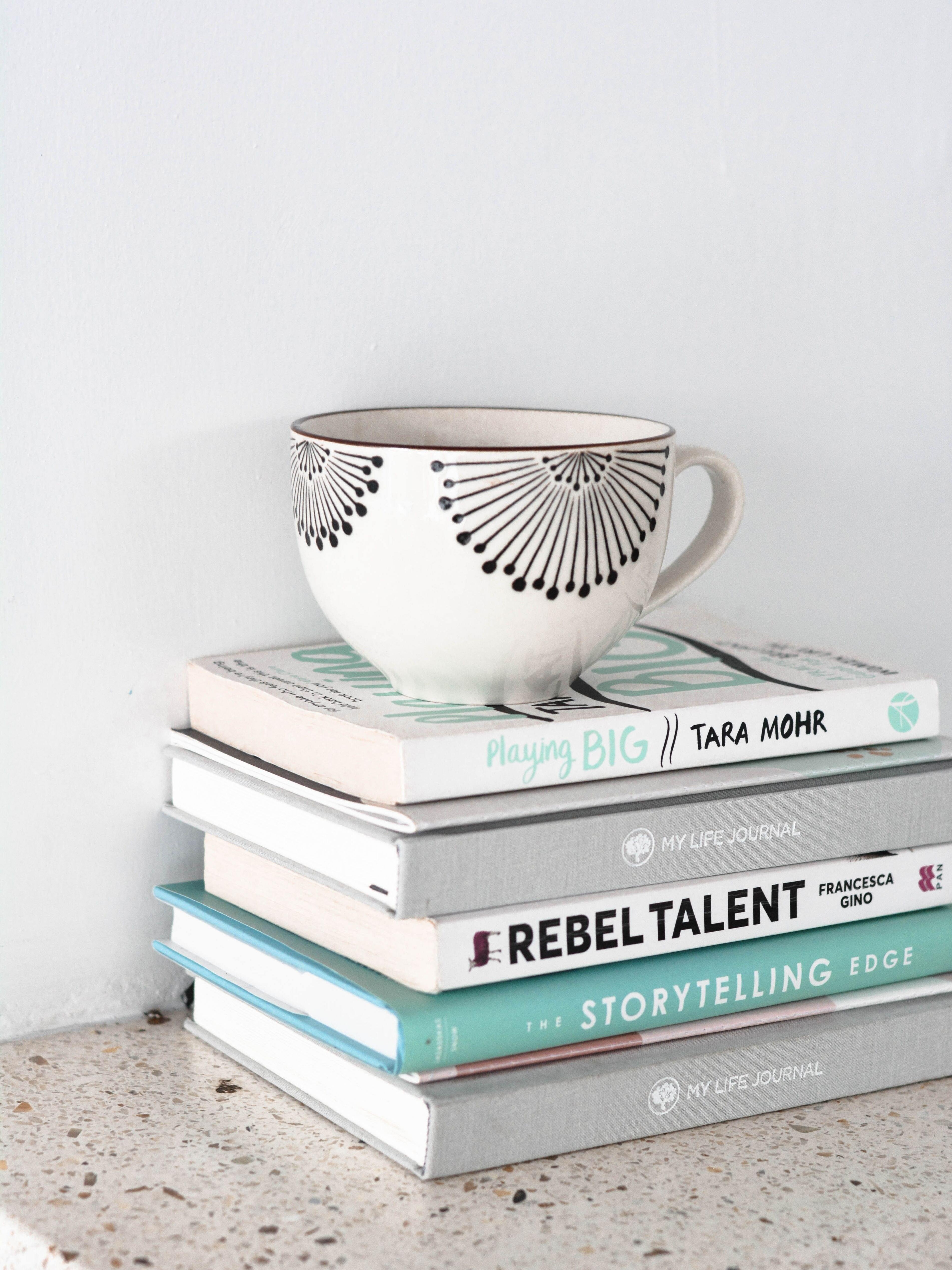 a pile of five books with a mug on top