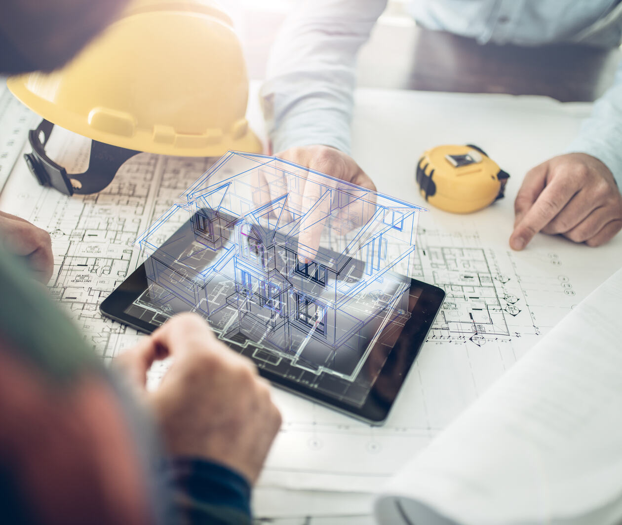 Architects sitting at a table looking at an iPad showing 3d architectural plans for a house.