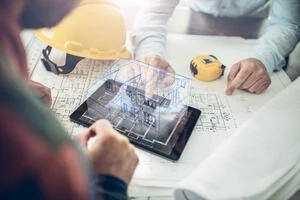 Architects sitting at a table looking at an iPad showing 3d architectural plans for a house.