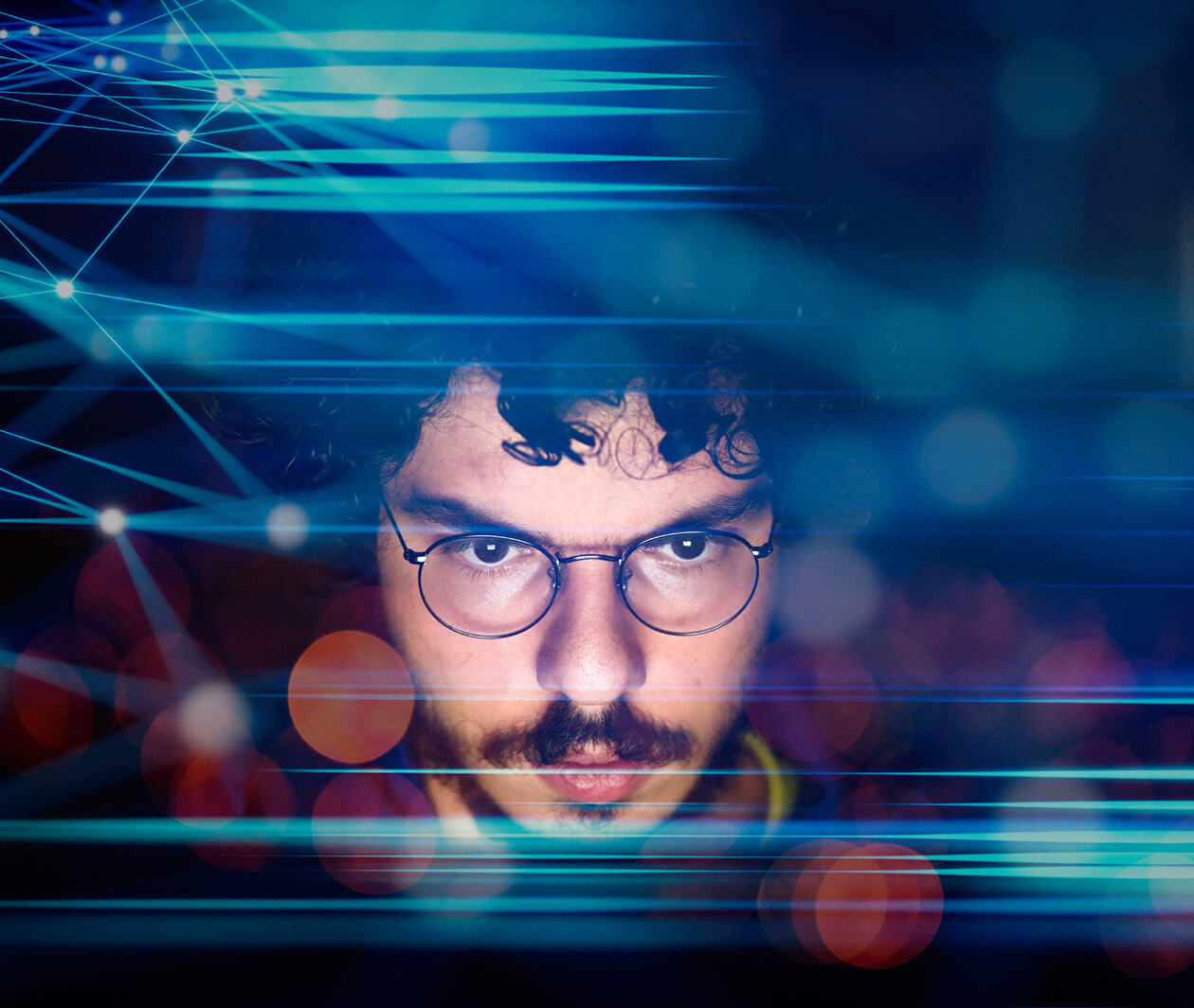 A young male computer programmer looking at his computer with overlay abstract finance economic graphs in the foreground.