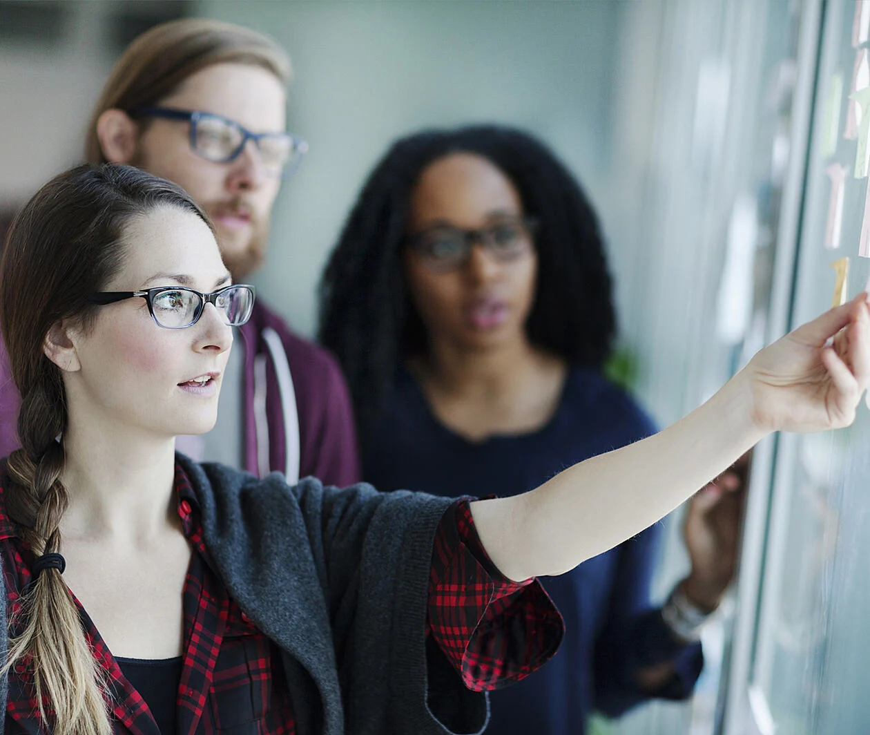 Three people looking at a screen with post-its on it. One person is reaching towards one of the post-its.