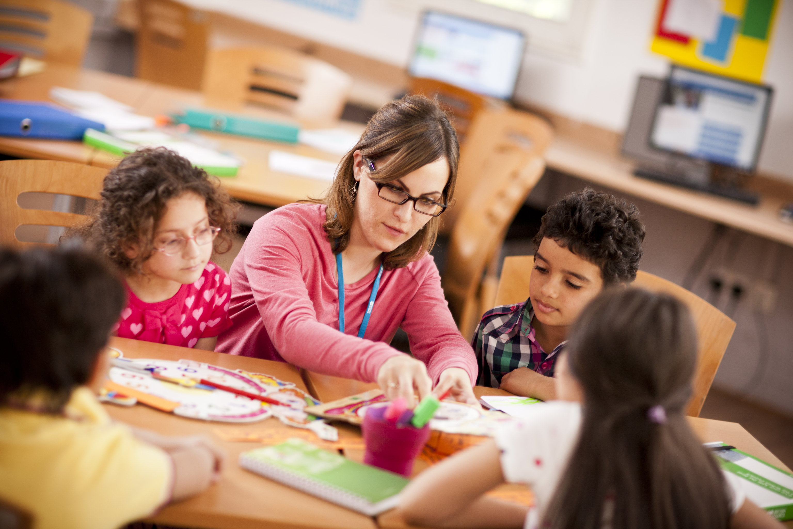 A teaching sitting with a group of children at a table teaching them.