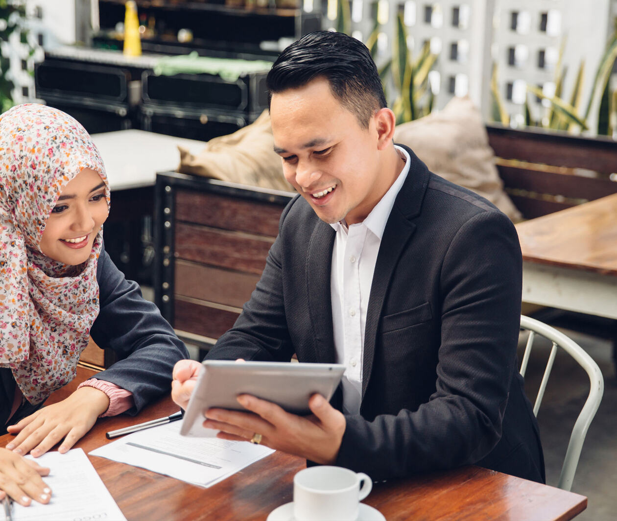 A financial adviser holding a tablet to show his Islamic client some digital banking products.