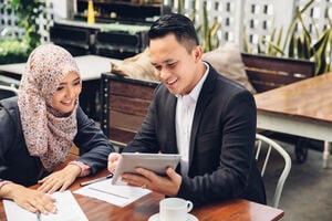 A financial adviser holding a tablet to show his Islamic client some digital banking products.