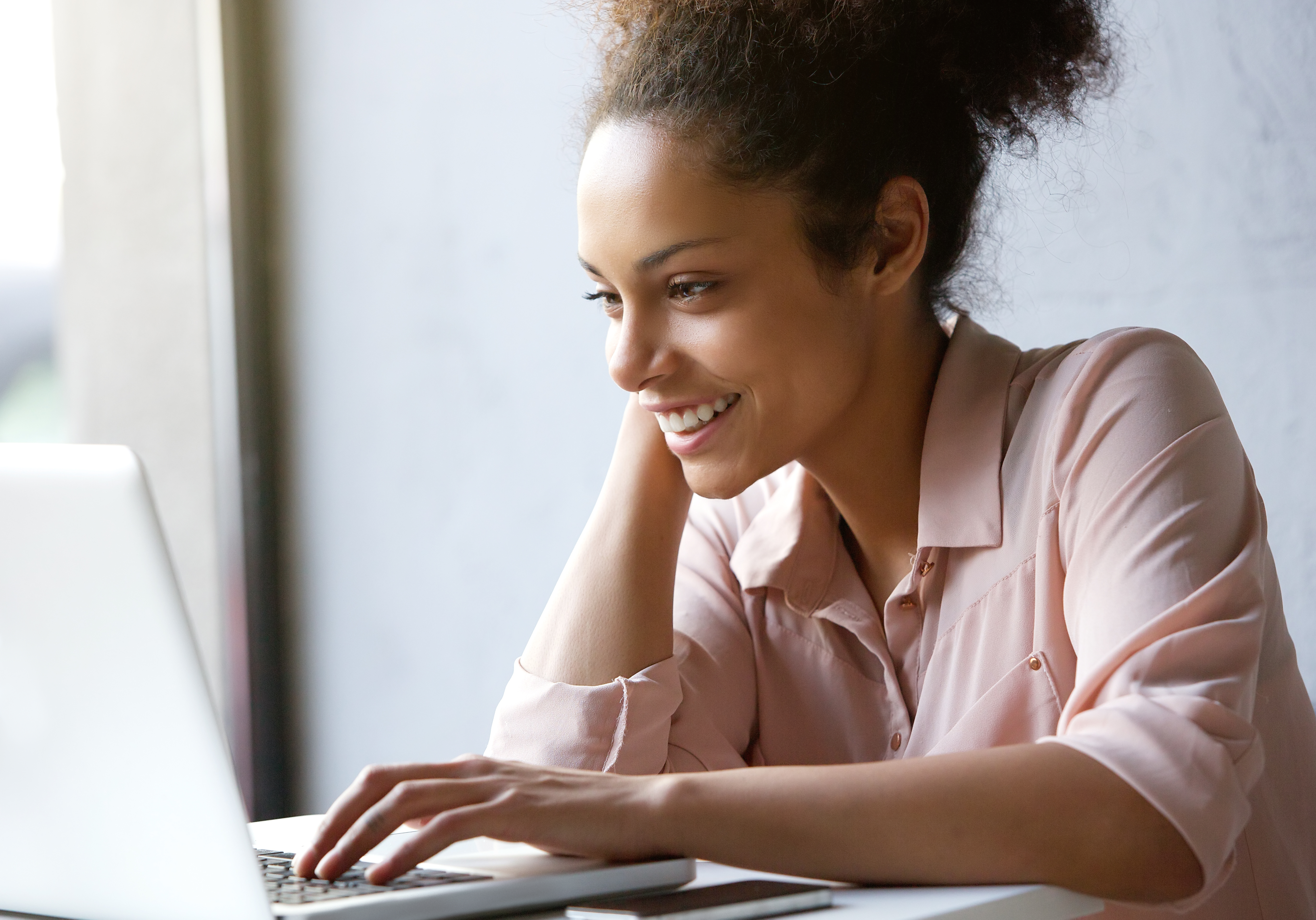 A young woman smiling as she reads on her computer.