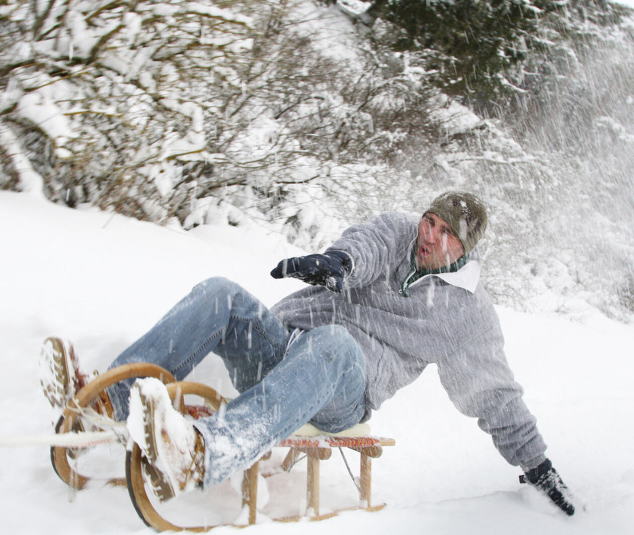 A man on a wooden sledge in the snow reaching out his arms to find his balance.