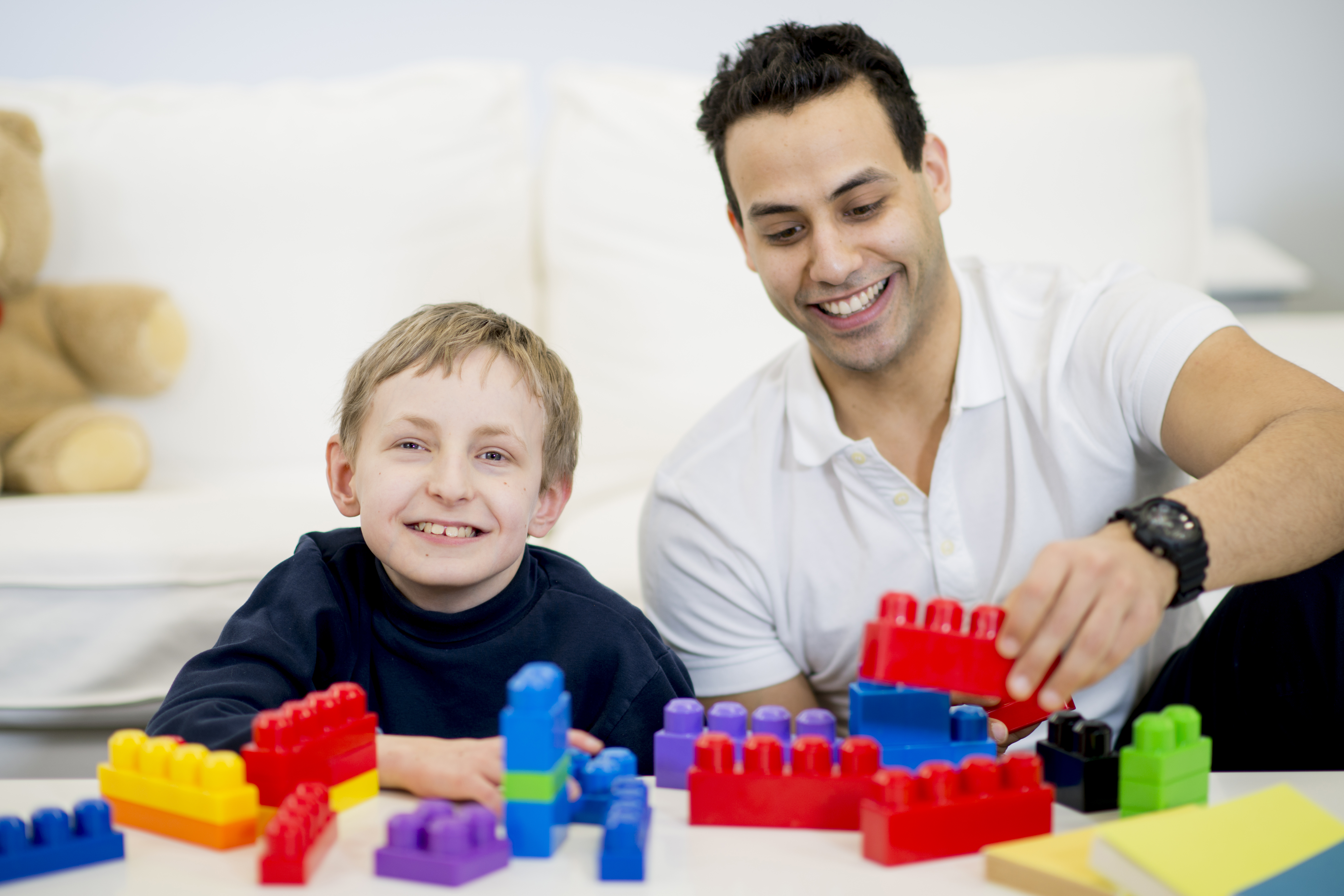 Male social care worker and child playing with lego building blocks and smiling