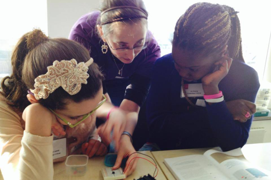 A woman showing two girls some electronics.