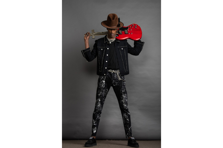 Man dressed in black with a brown hat, facing the camera holding a red guitar