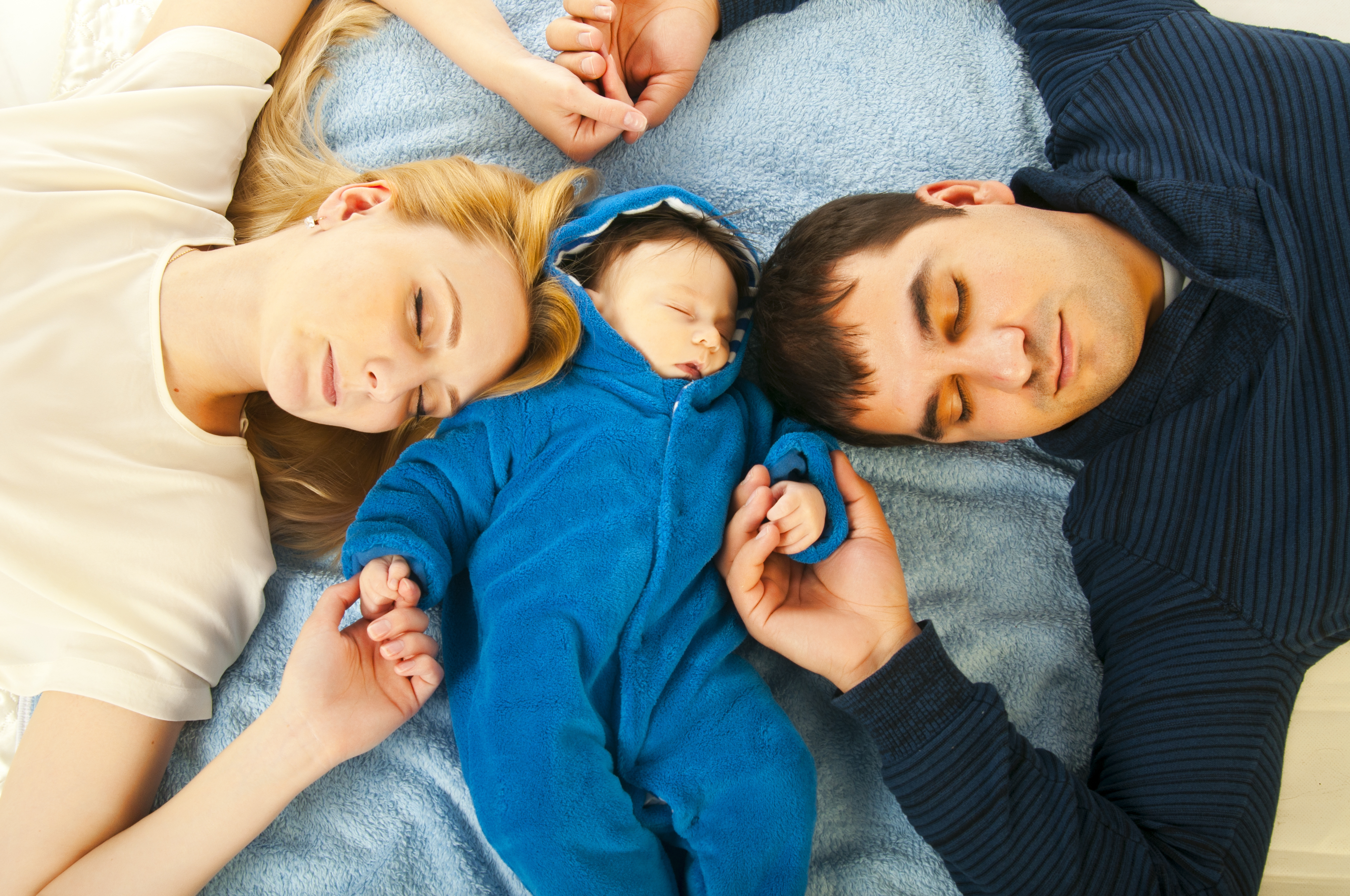 A man and a woman lying down and holding their baby's hands.