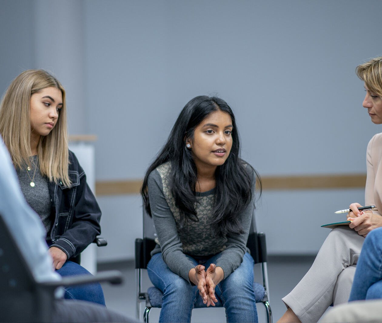 A diverse group of teenagers sit in a group therapy circle with a councillor supporting their mental health and wellbeing.