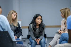 A diverse group of teenagers sit in a group therapy circle with a councillor supporting their mental health and wellbeing.