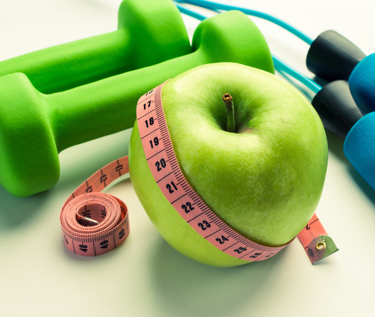 Green apple with hand weights, waist measure and skipping rope