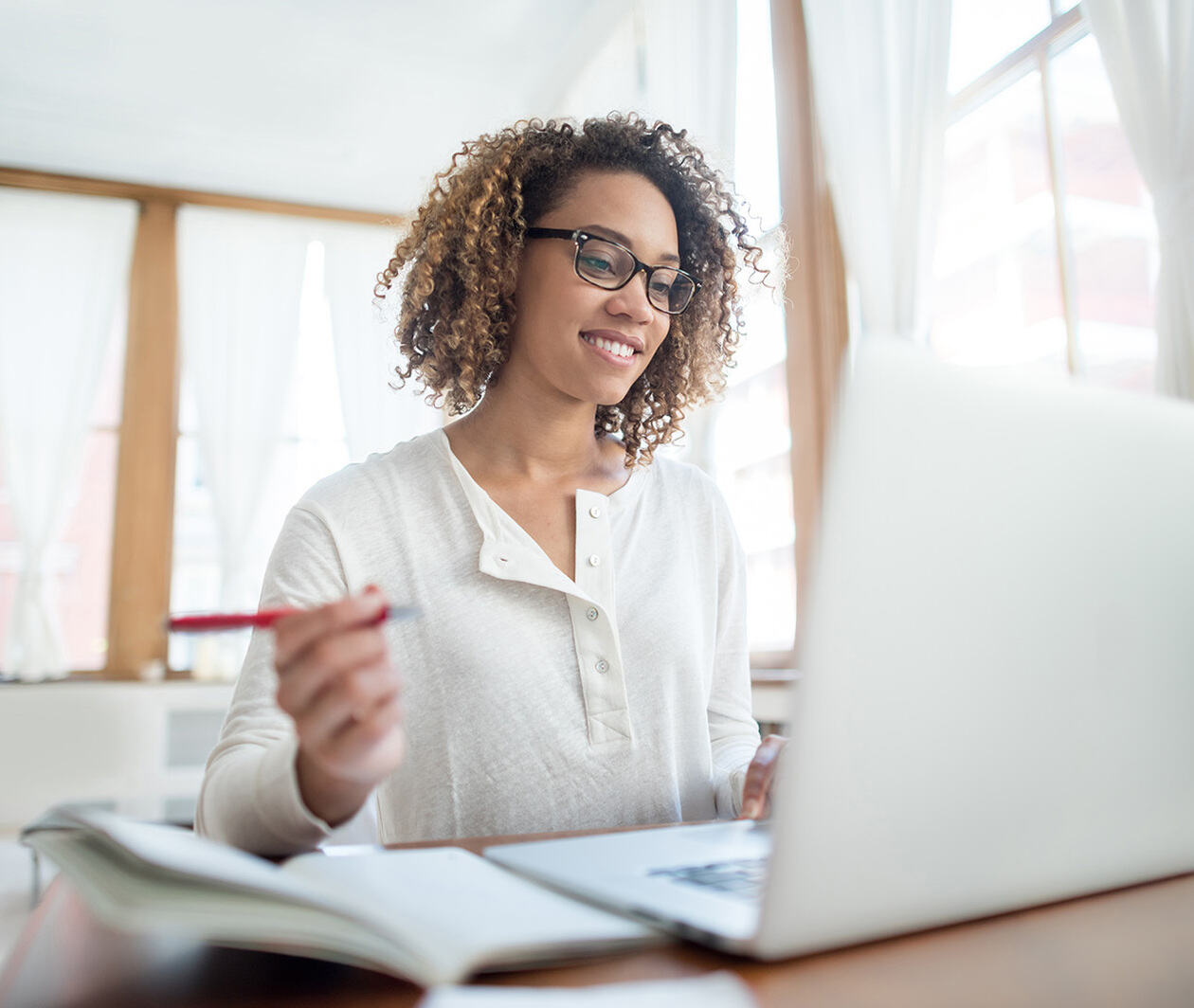 A woman smiling whist looking at a laptop and writing on a notepad.