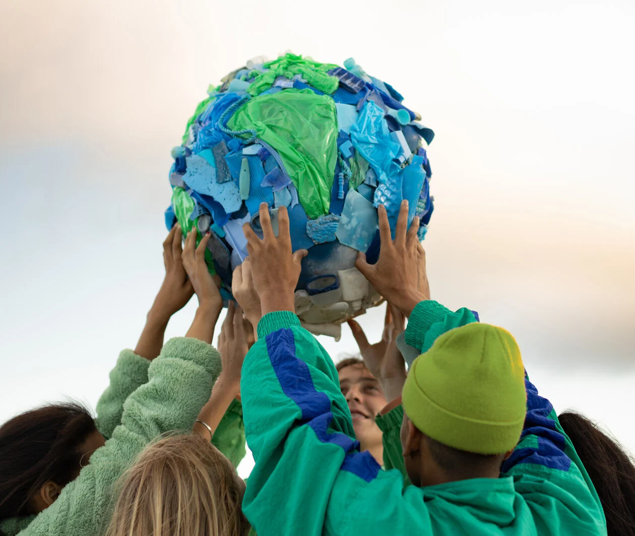 Group of people wearing green holding up a globe made of recycled plastic