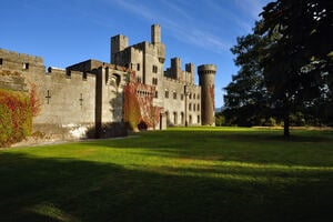 彭林城堡（Penrhyn Castle）在阳光明媚的日子里，前面有绿草和树木，明亮的蓝天。