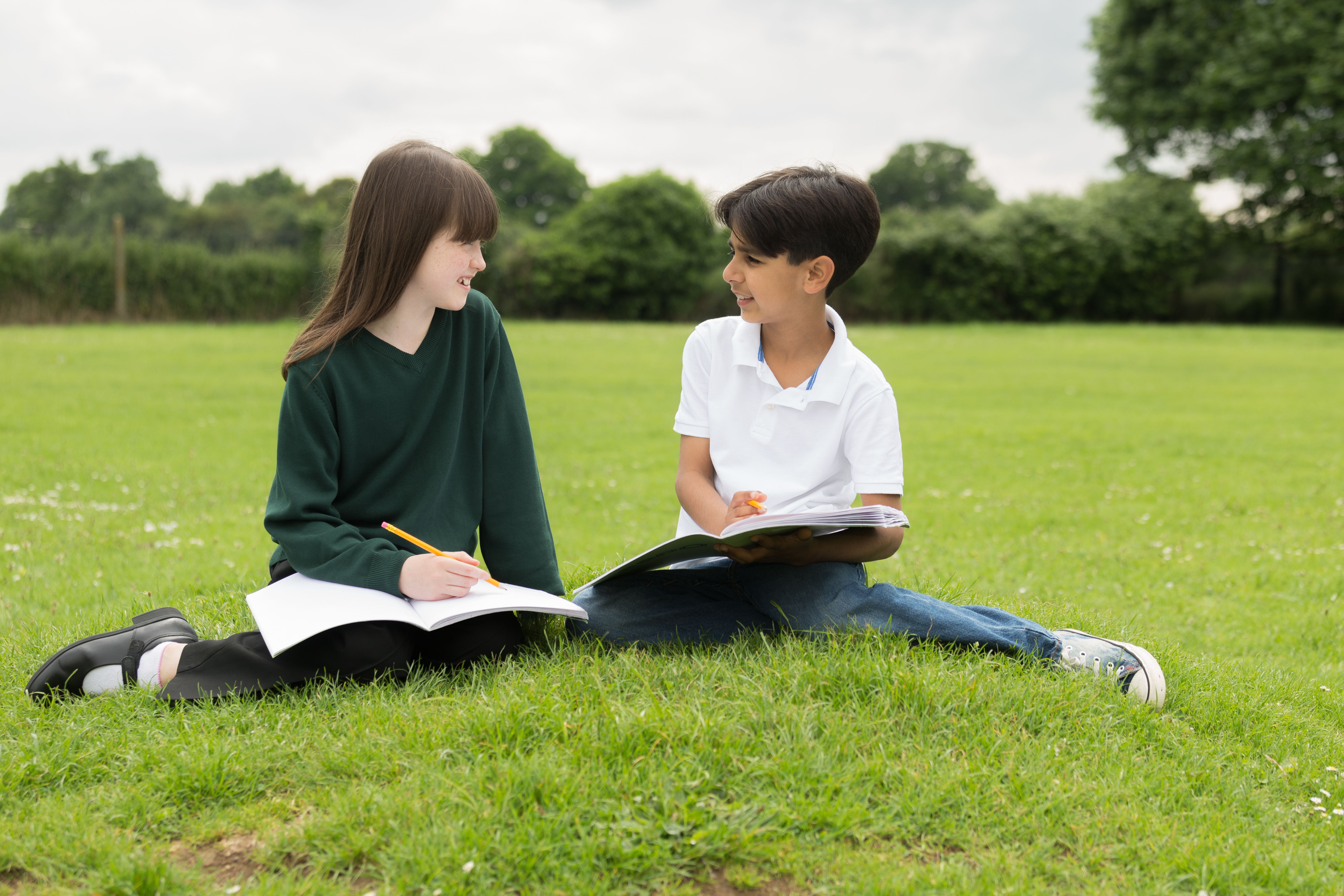 two students writing in books on a grass lawn