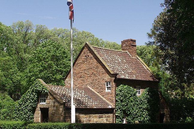 Photo of Cook's cottage, Melbourne, a redbrick cottage covered in ivy set in trees with flagpole outside carrying union jack
