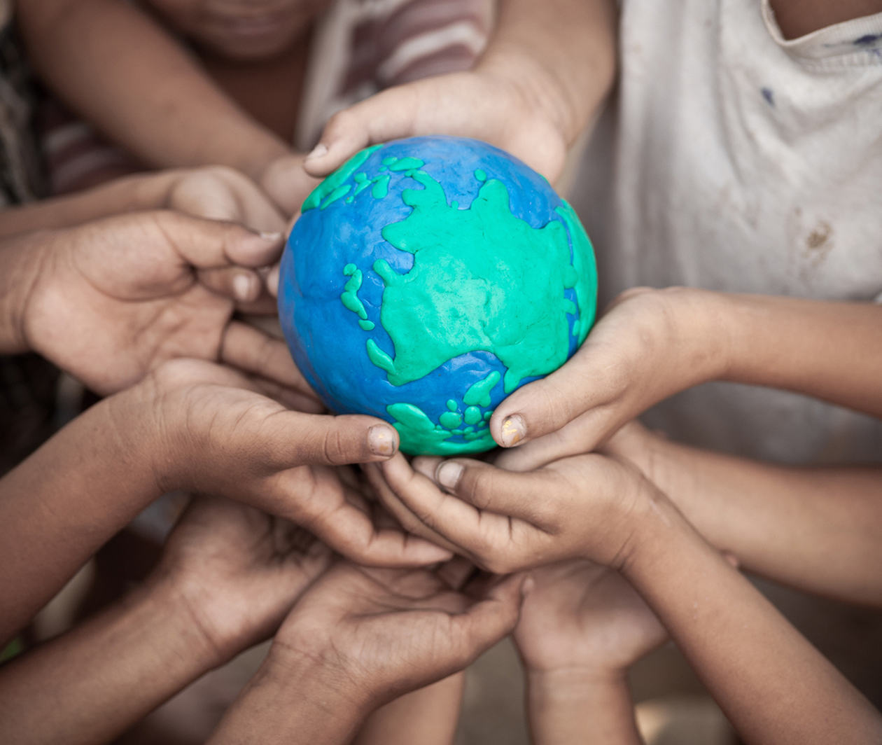 Children's hands holding a globe made of plasticine.