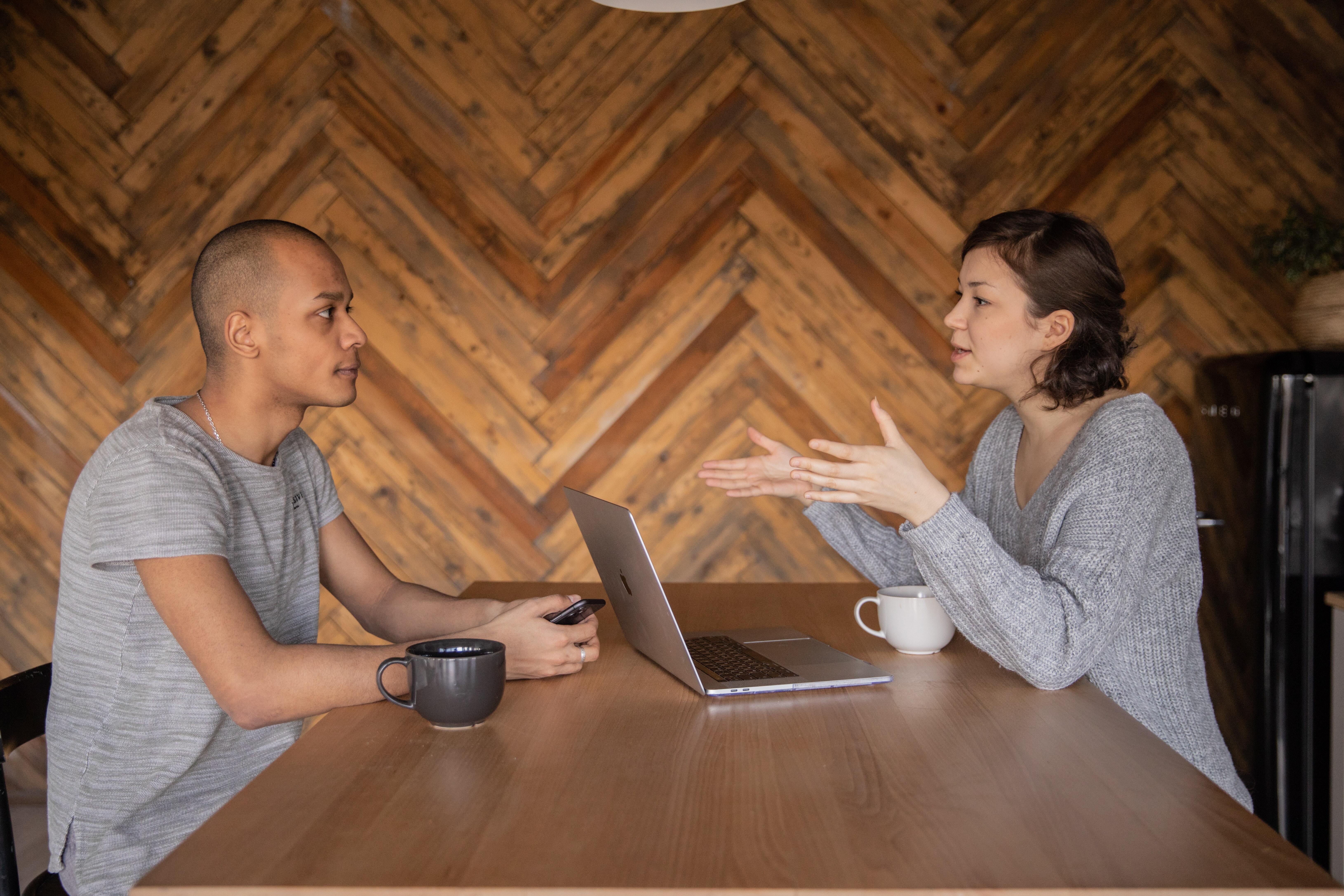 Two individuals sitting on either side of a table having a conversation.