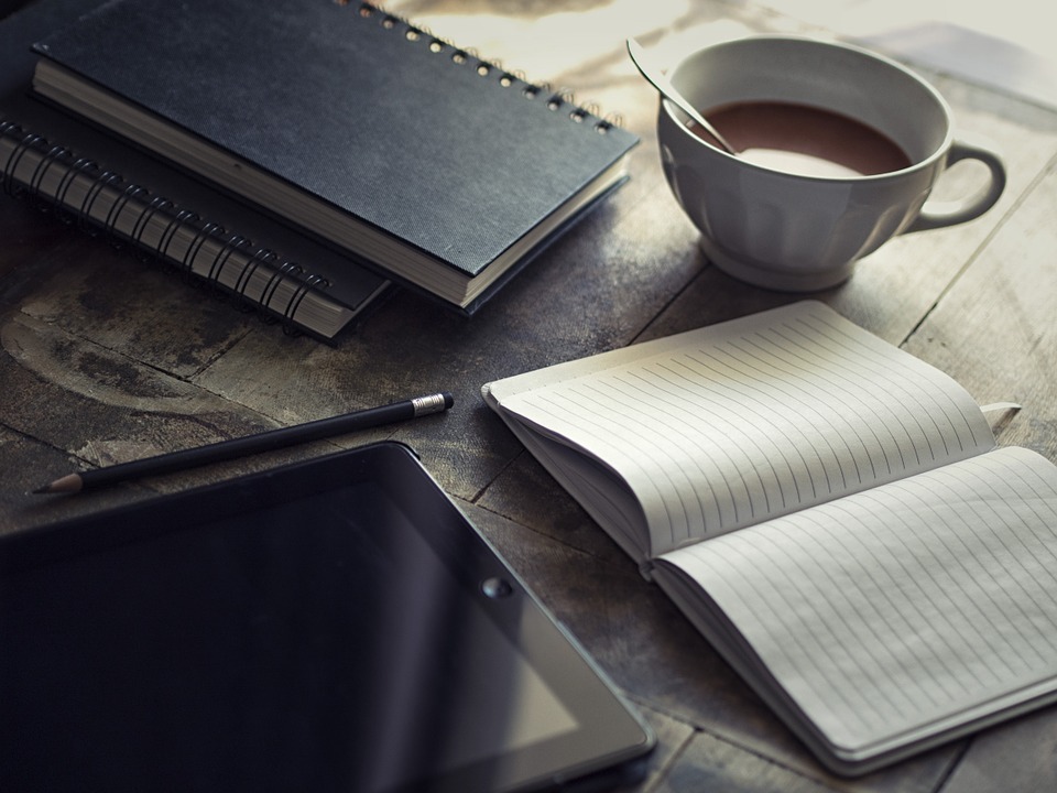 Image of a notepad, ipad and coffee on a desk