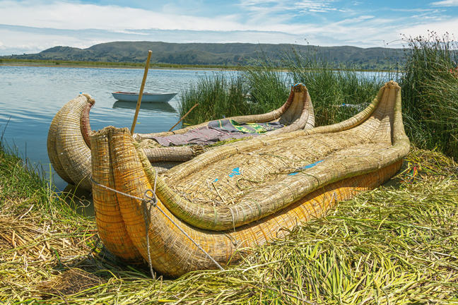 An image of two reed boats on the shore of a lake.