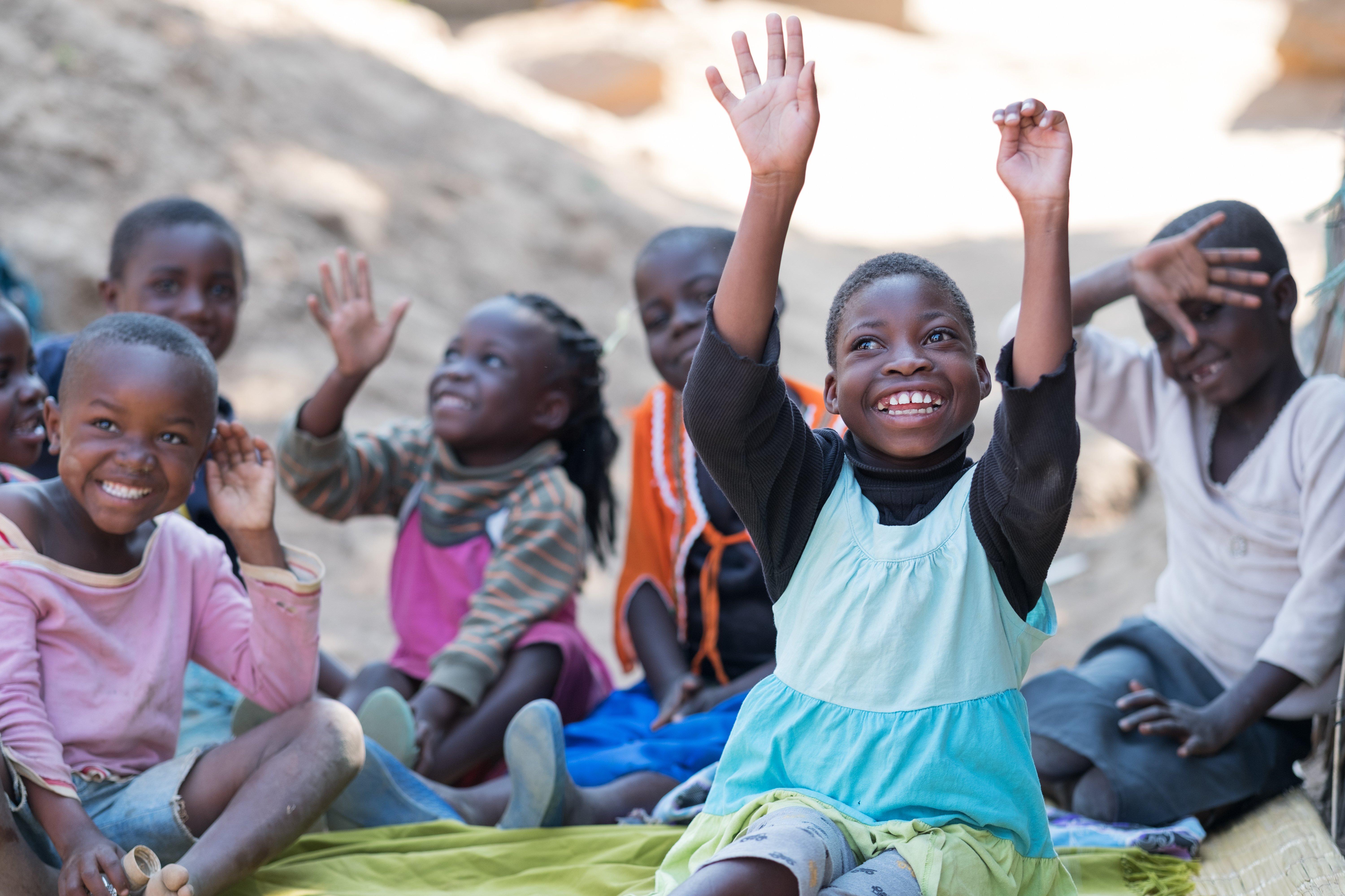 A girl with cerebral palsy sits with friends. She has her hands in the air as she smiles