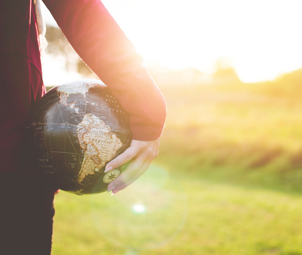 A person looks out on a field. They are holding a globe in one hand.