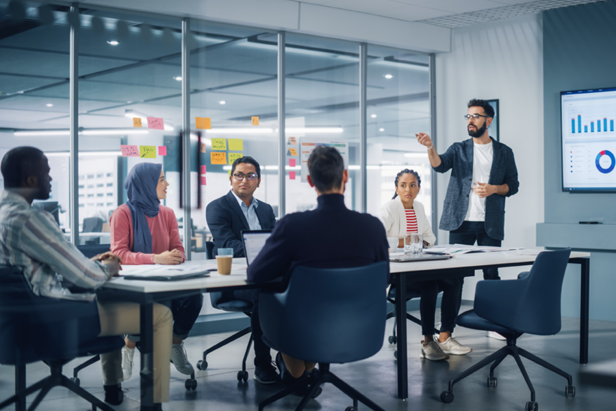 Diverse Modern Office: Businessman Leads Business Meeting with Managers, Talks, uses Presentation TV with Statistics, Infographics. Digital Entrepreneurs Work on e-Commerce Project.