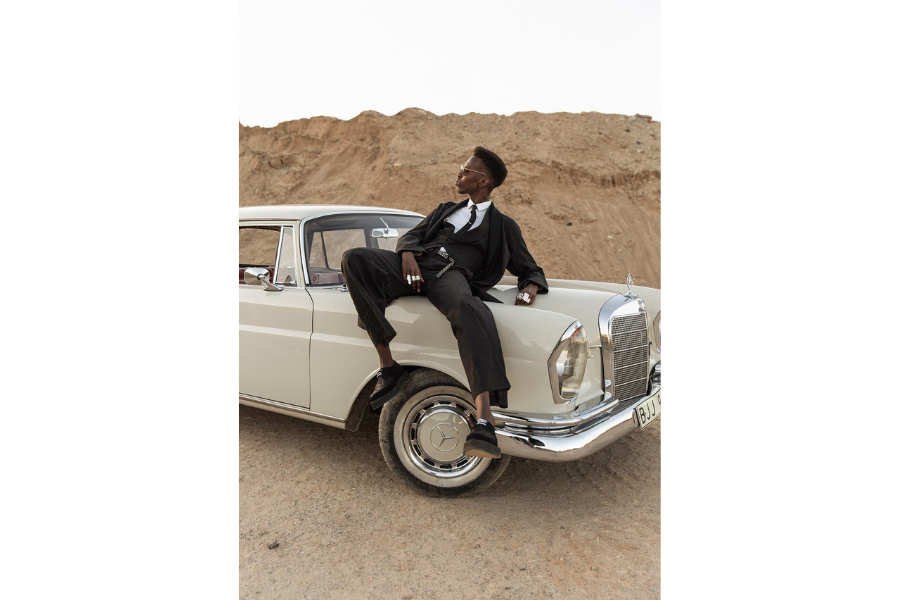 A person sat on a vintage car in a desert, facing the left.