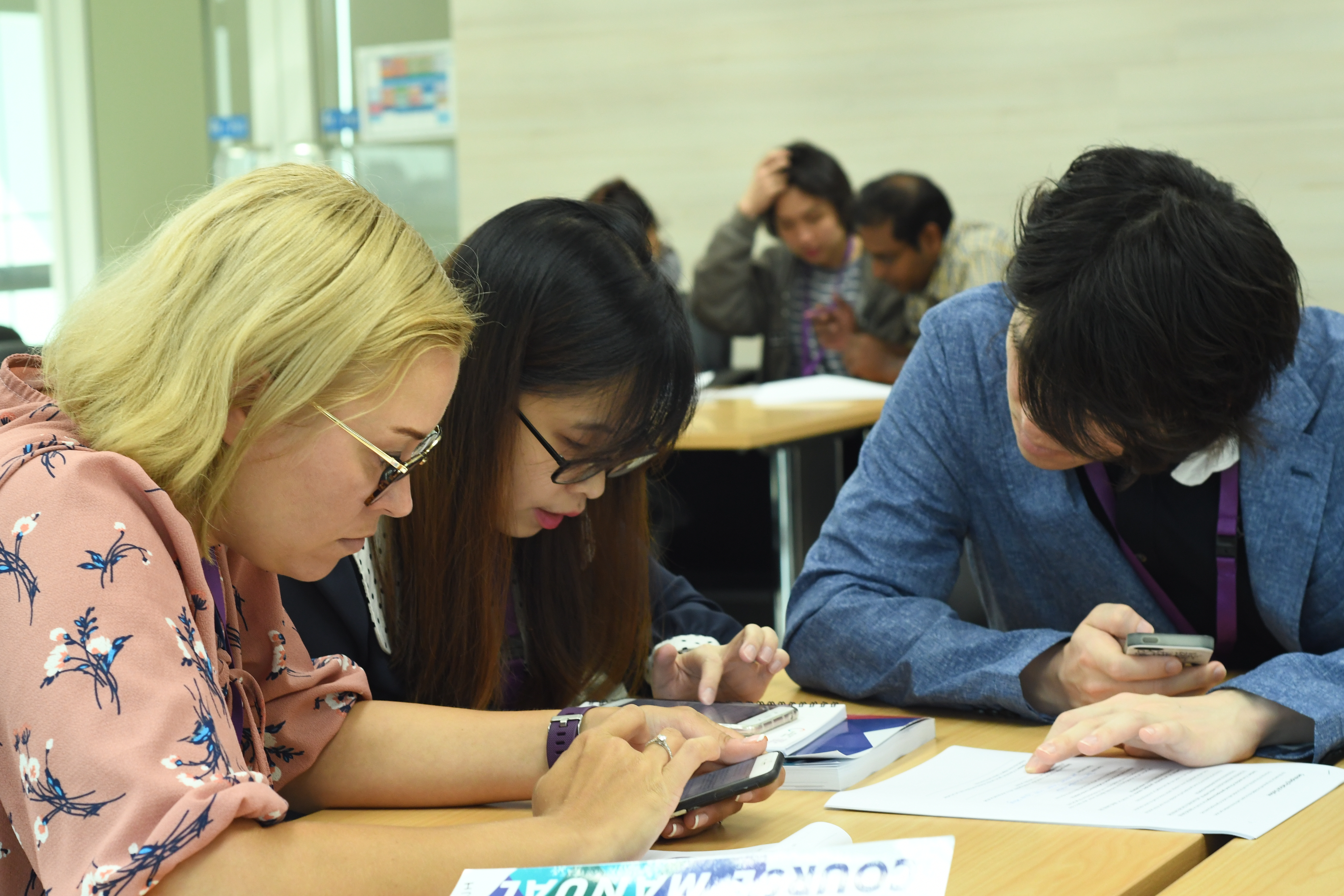 three learners working together sitting at a table and using their phones/calculators