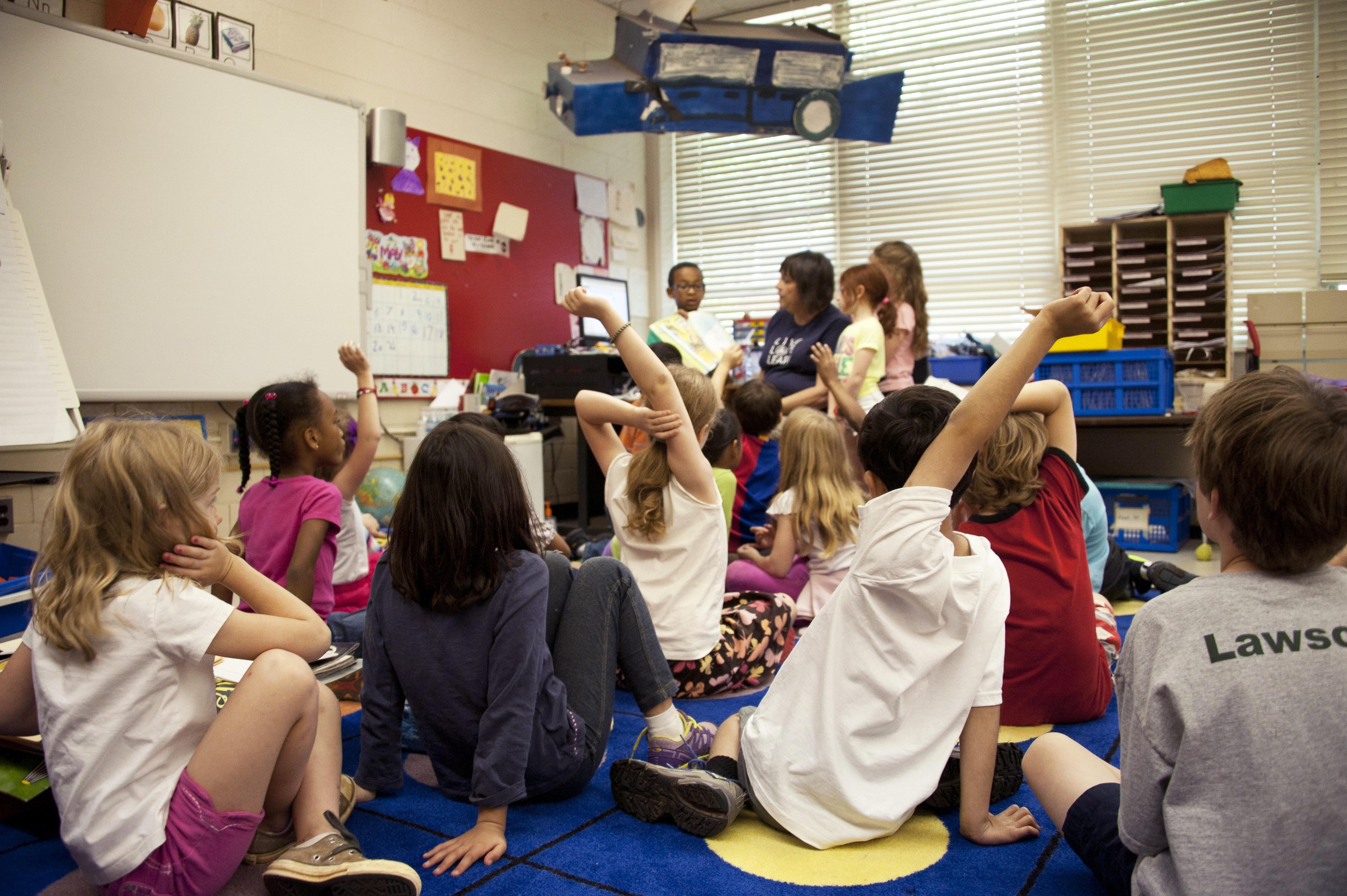 Pupils sitting around a teacher in class, some with their hands up