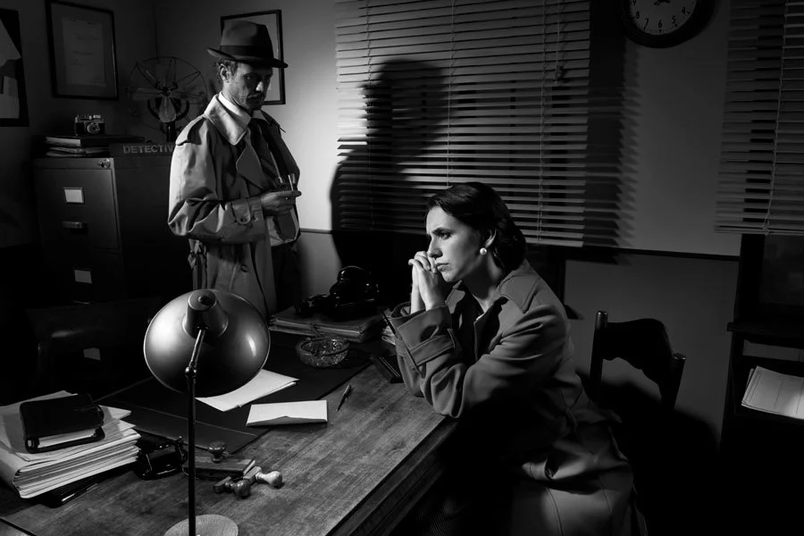 Pensive woman being interviewed at desk by detective in a noir setting