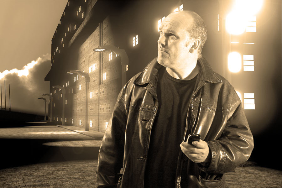 Man in a leather jacket holding a mobile phone at night outside a building with streetlights outside