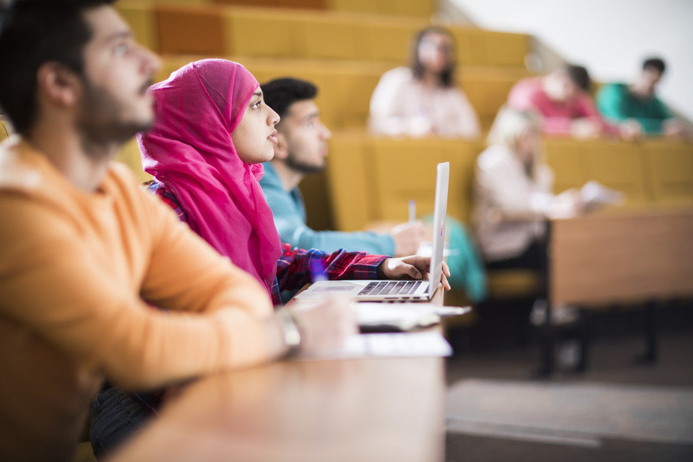 A group of students sitting with their laptops and notebooks, listening in a lecture theatre