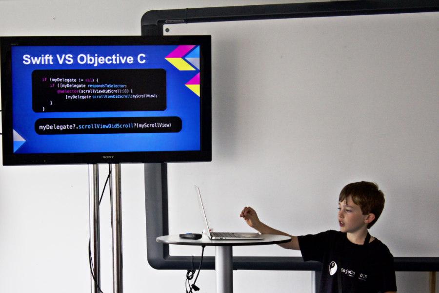 A boy in a CoderDojo t-shirt is delivering a lesson, with slides, on coding.