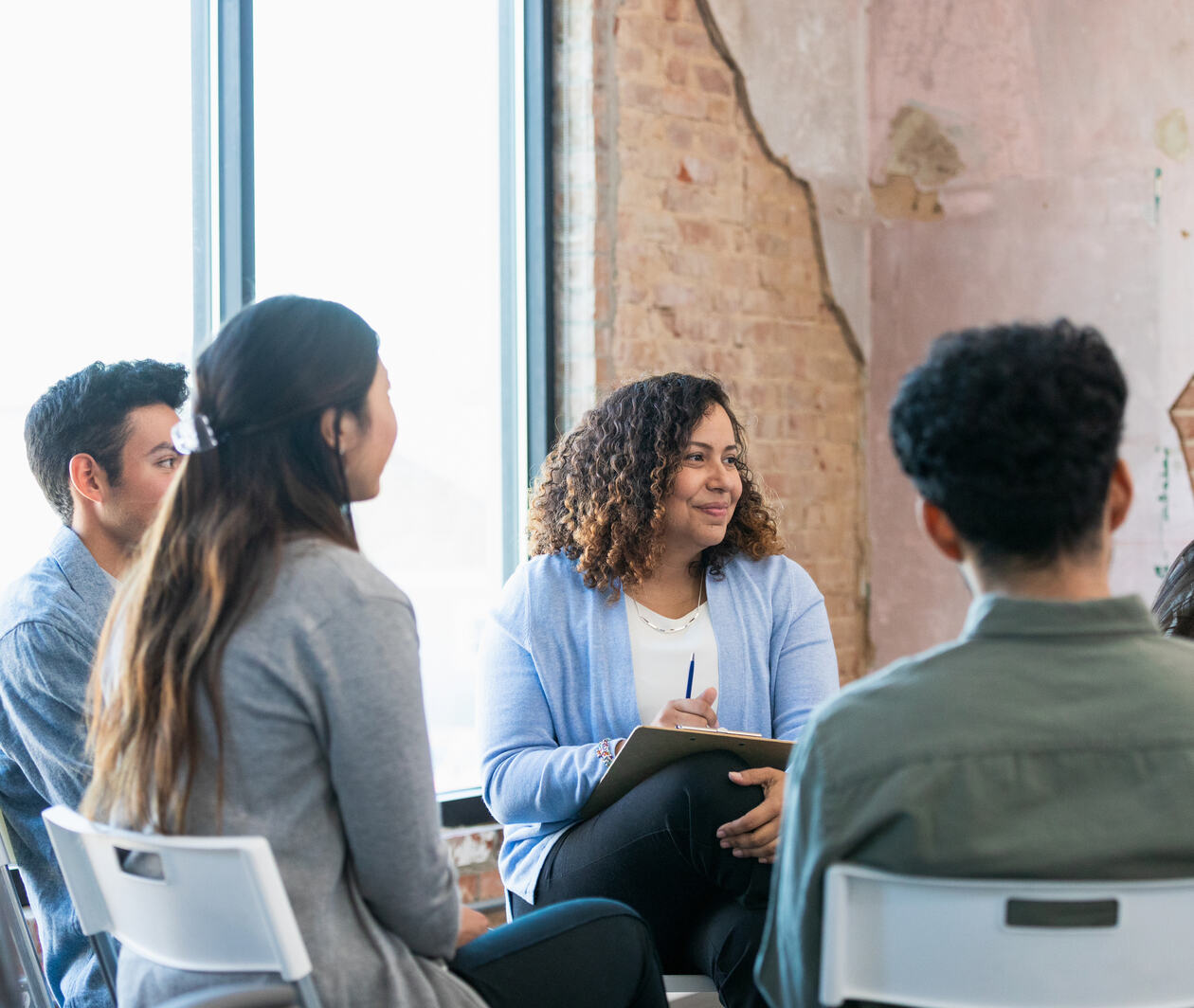 The diverse therapy group listens attentively as the young adult woman shares.